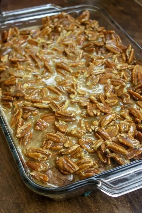 A tray of pecan pie brownies with a shiny glaze and golden pecans on top.