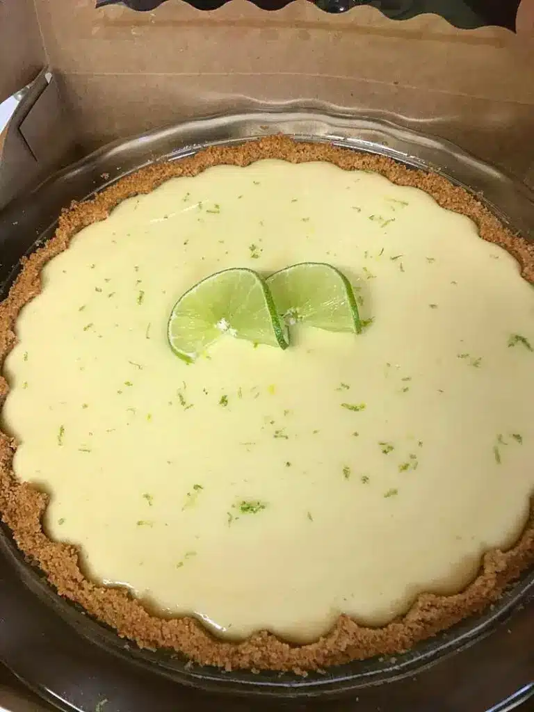 A whole key lime cheesecake garnished with lime slices and whipped cream dollops.