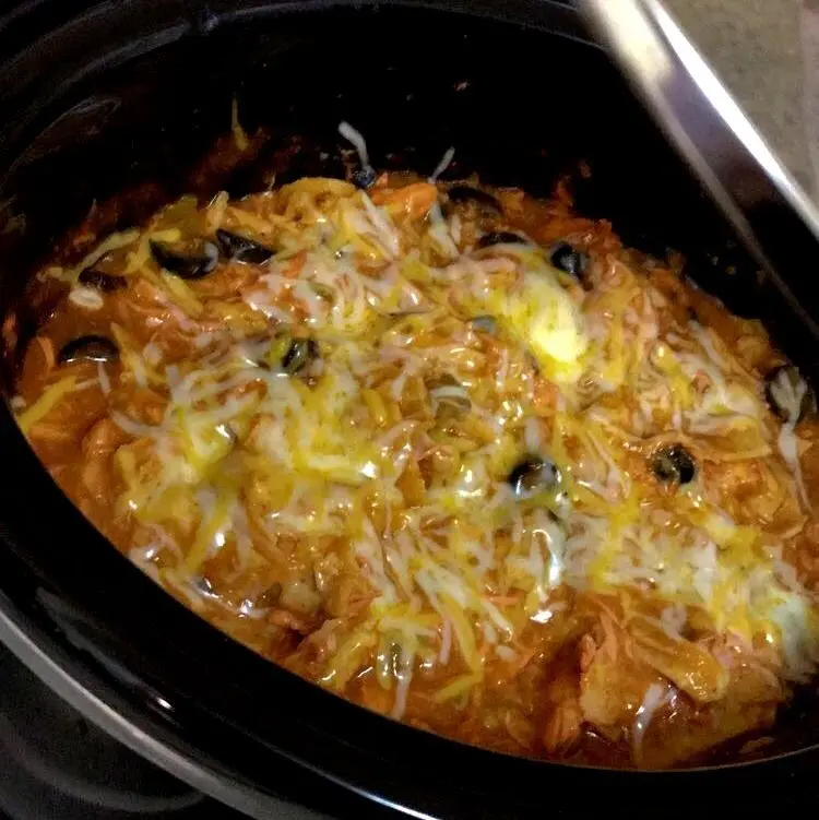 Serving a scoop of crock pot chicken enchilada casserole with sour cream and lime
