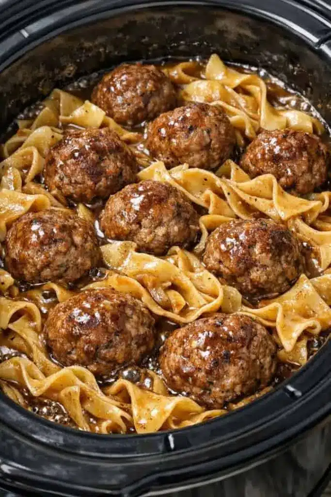 A bowl of Amish meatball noodles served with a side of green beans and a dinner roll