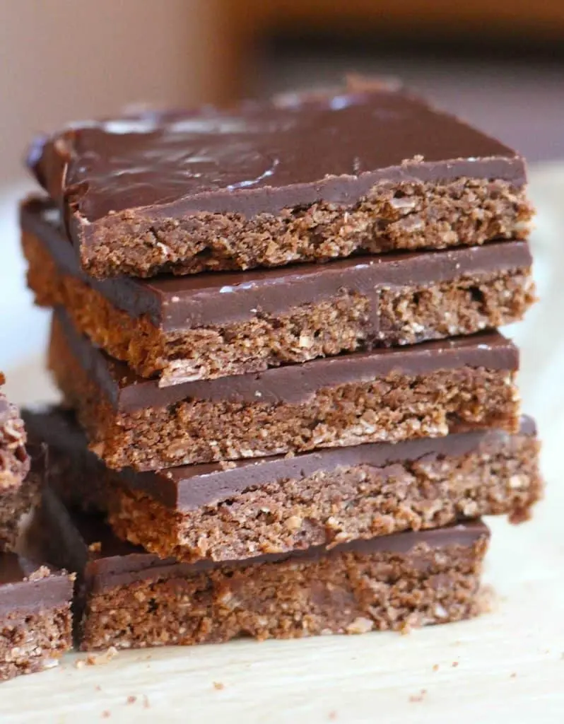 Individual squares of chocolate biscuit slice arranged on a white plate with a cup of tea.