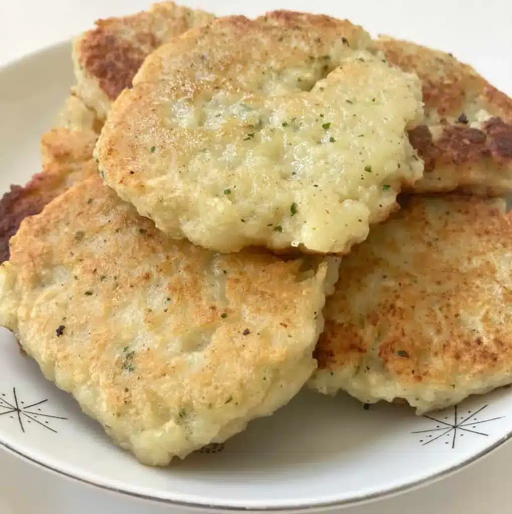 A stack of golden brown Amish potato pancakes served with a side of applesauce and sour cream.