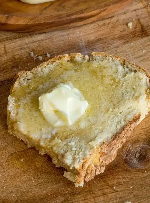 Slices of Irish soda bread served with thick yellow butter and a side of berry jam on a rustic table.