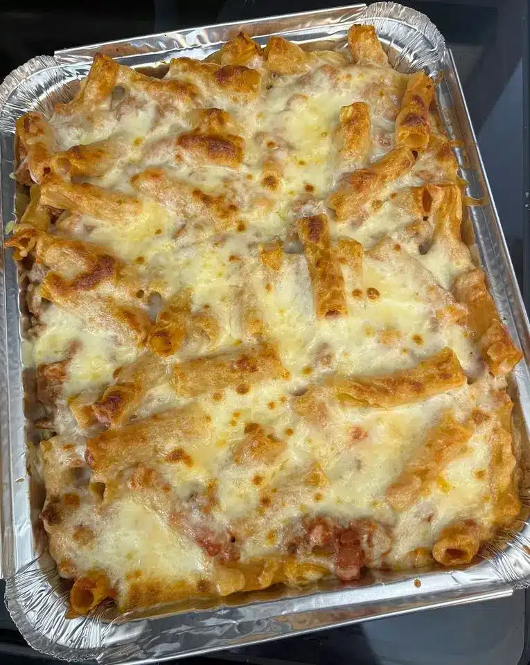 A serving of baked pasta on a white plate with a side salad and a glass of red wine