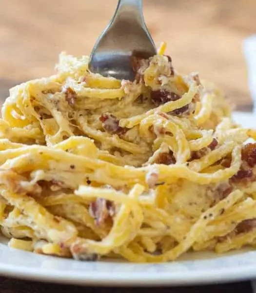 A serving of bacon cream cheese baked spaghetti on a white plate with parsley garnish