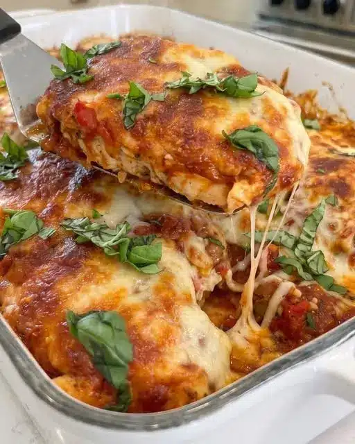 A serving of chicken mozzarella casserole on a plate next to a side of pasta.