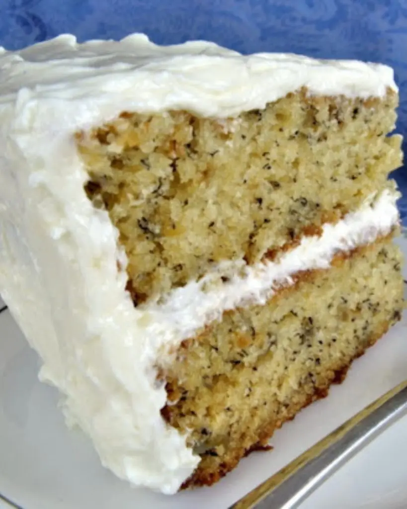 A slice of banana cake with thick buttercream frosting being served on a white plate with a fork.