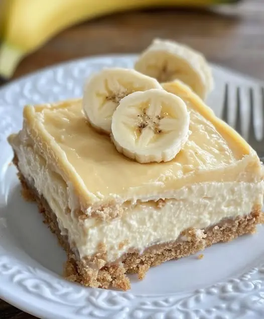 A close up of a sliced banana cream cheesecake bar showing the distinct layers