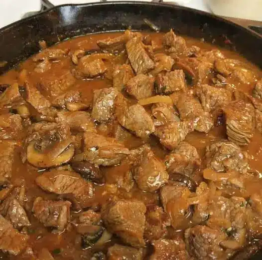 Beef tips and gravy garnished with fresh parsley served in a bowl over white rice.