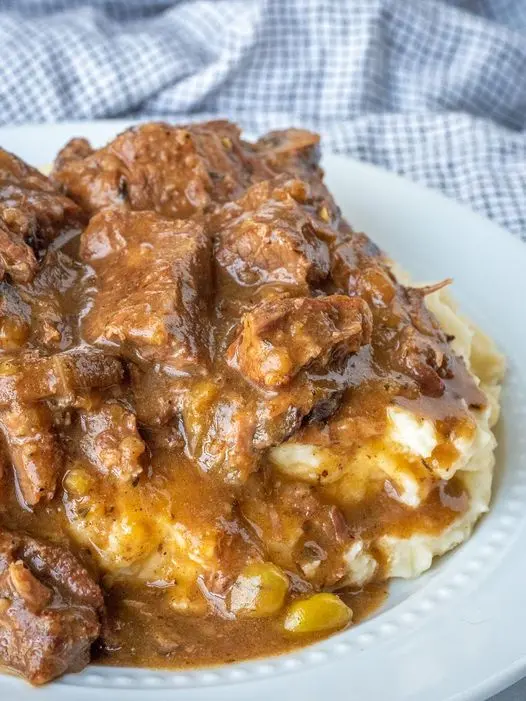 A bowl of beef tips and mushroom gravy served over creamy mashed potatoes garnished with fresh parsley.