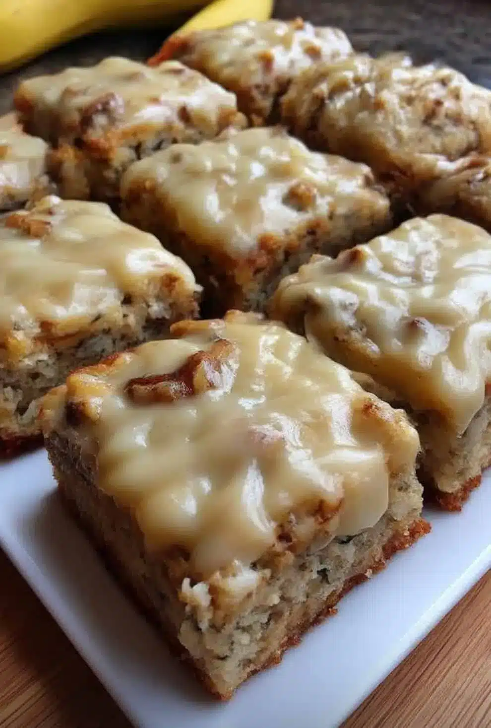 Sliced banana bread brownies topped with a creamy glaze and served on a white plate