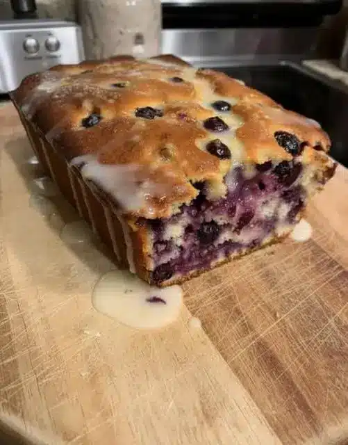 A slice of blueberry quick bread served on a plate with a pat of butter, showing the moist interior and berry distribution.