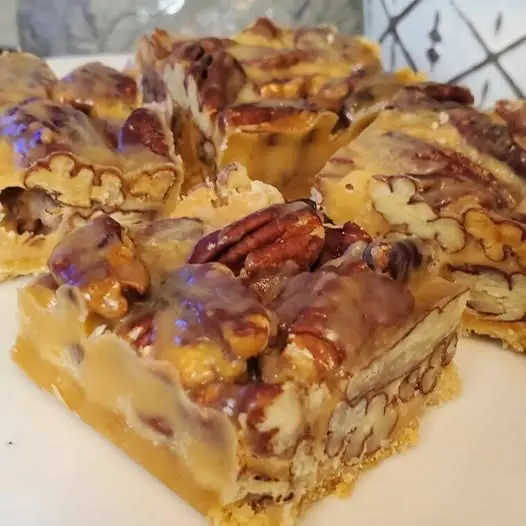 sliced caramel pecan bars stacked on a plate showing the layers of shortbread and pecans