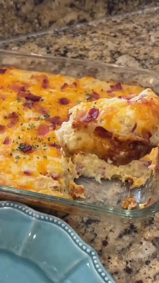 A sliced square of cheesy breakfast casserole served on a white plate with fresh fruit.