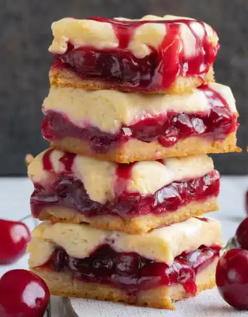 A single cherry cheesecake bar on a white plate showing the creamy layers.