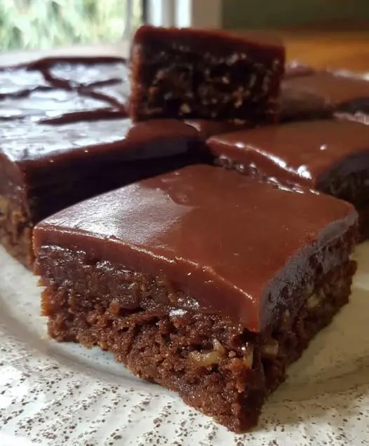 Slices of chocolate sheet cake on a serving plate with a glossy chocolate finish