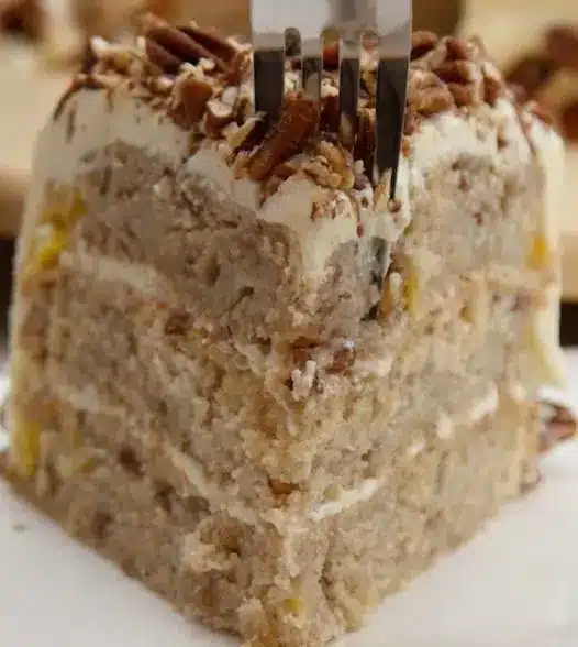 A slice of hummingbird cake on a plate showing the moist fruit and nut interior and creamy frosting