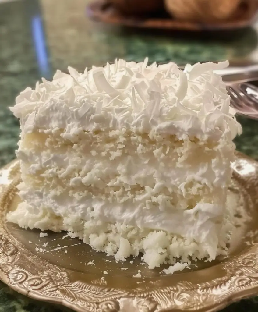A slice of moist coconut poke cake topped with toasted coconut