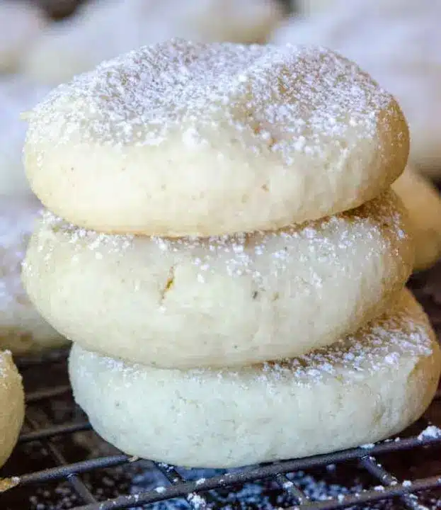 A stack of soft cream cheese cookies on a white plate next to a cup of coffee.