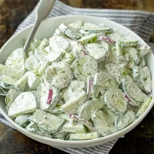 A finished bowl of creamy cucumber salad garnished with fresh dill