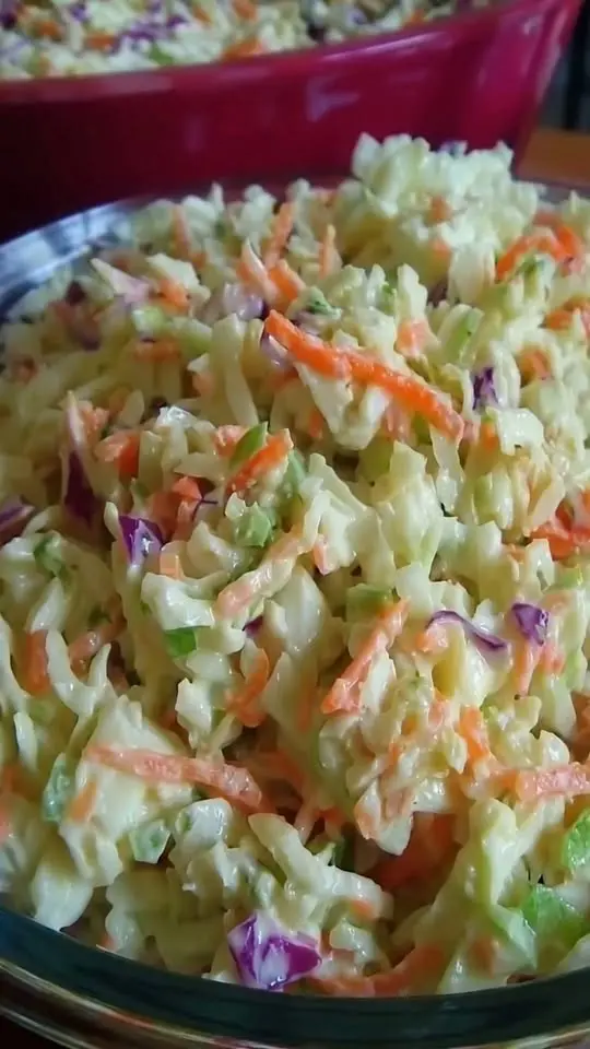 A close-up shot of creamy coleslaw served in a white bowl alongside a barbecue sandwich