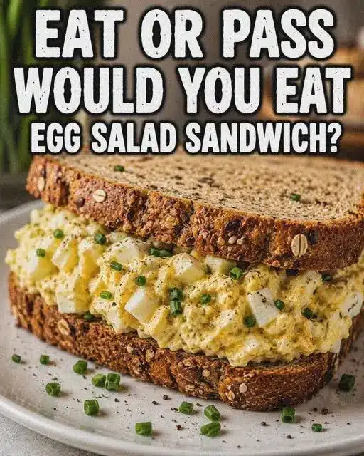 Two egg salad sandwiches sliced in half and stacked on a plate with potato chips