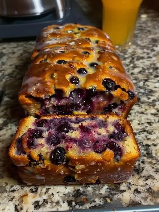 A whole loaf of blueberry bread on a wooden board with fresh blueberries scattered around