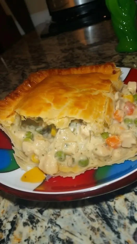 A golden slice of chicken pot pie served on a plate with steam rising from the creamy filling