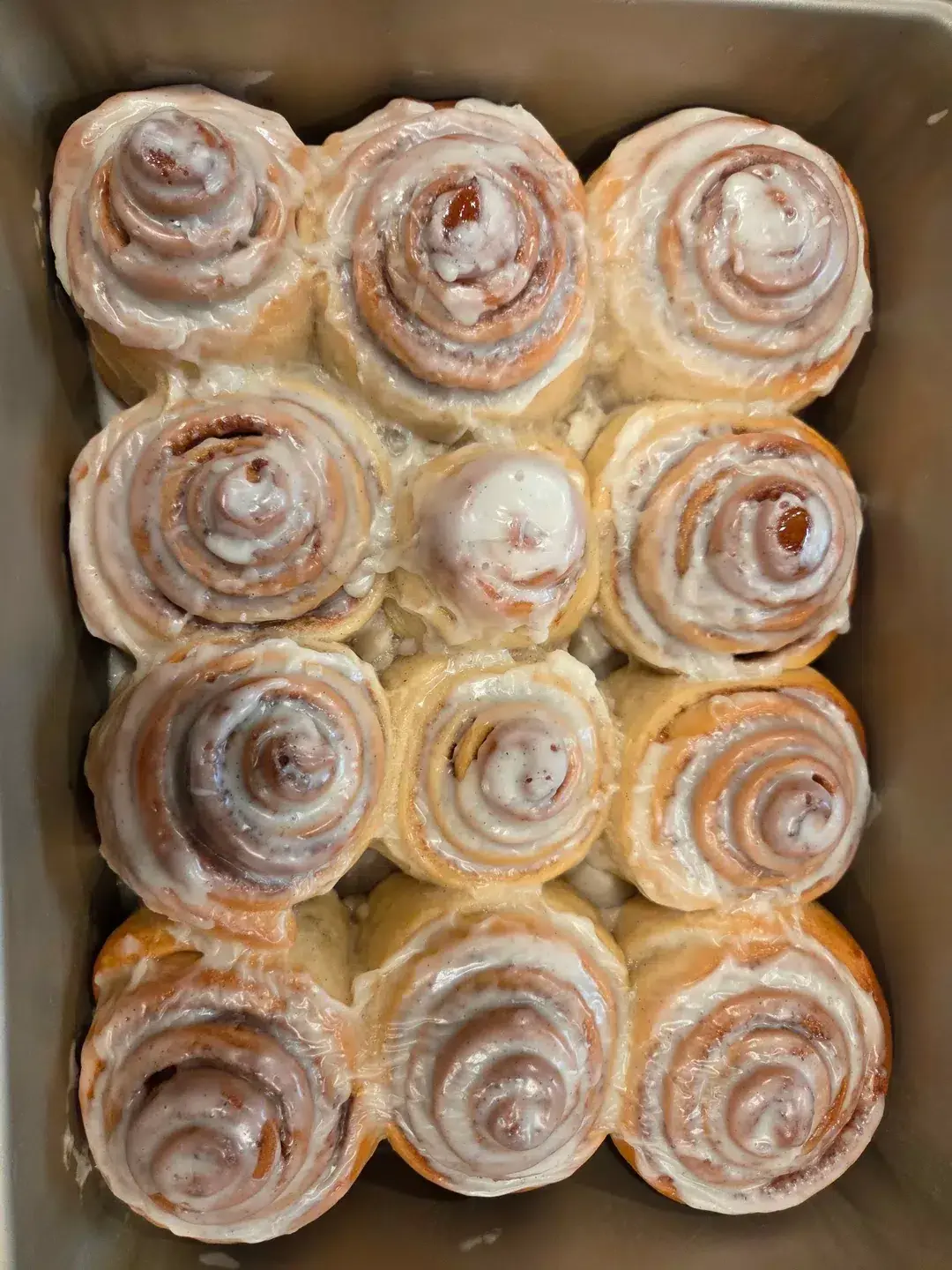 A single warm cinnamon roll with melting cream cheese frosting on a white plate