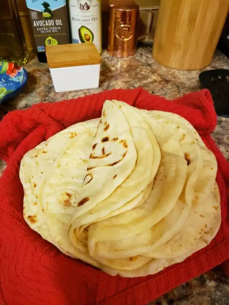 A stack of fresh flour tortillas with charred spots on a plate