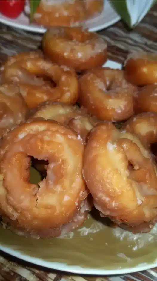 A stack of perfectly glazed, golden brown yeast donuts on a wire cooling rack