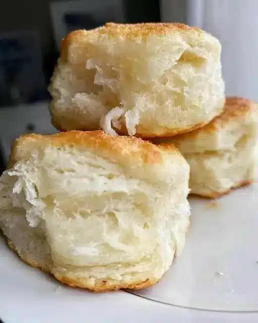 A basket of soft glazed dinner rolls served with a side of extra honey butter
