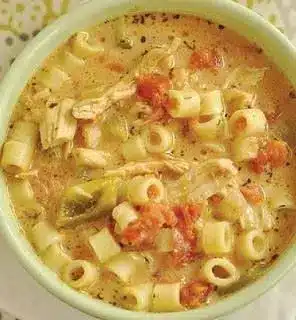 A close up of Italian chicken soup served with a side of crusty bread and a sprinkle of parmesan cheese.