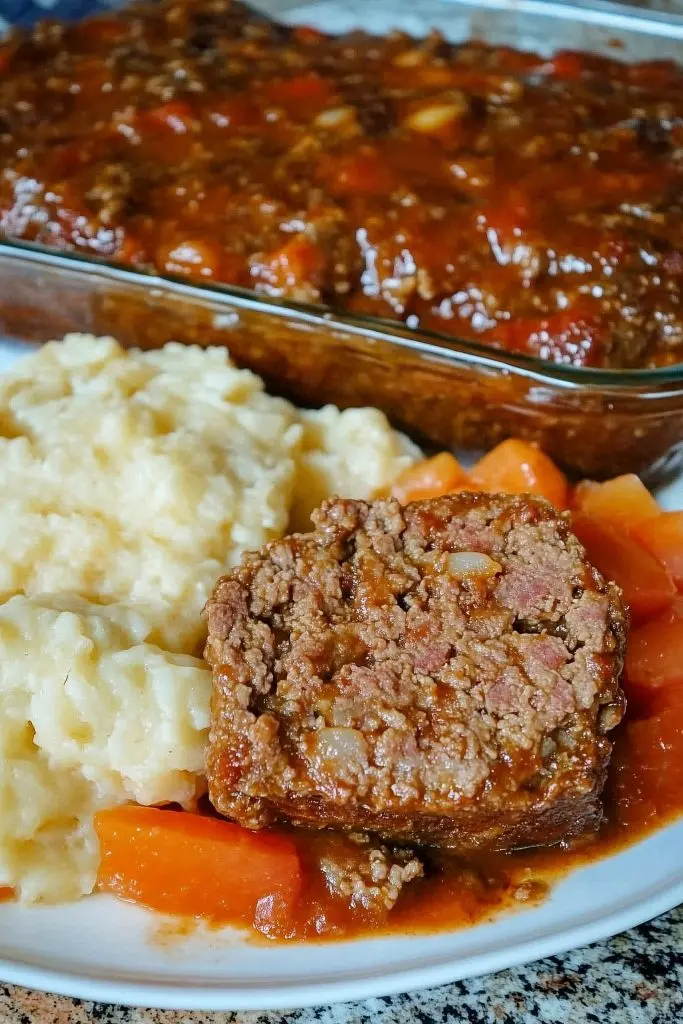A perfectly sliced meatloaf with tomato sauce served with mashed potatoes and green beans
