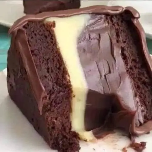 Two layers of chocolate cake with a thick layer of chocolate frosting being applied to the top.