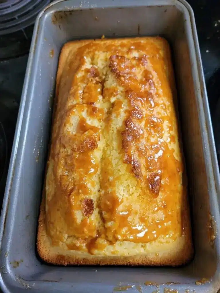 A sliced moist lemon cake on a white plate with a drizzle of lemon glaze and a sprig of mint.