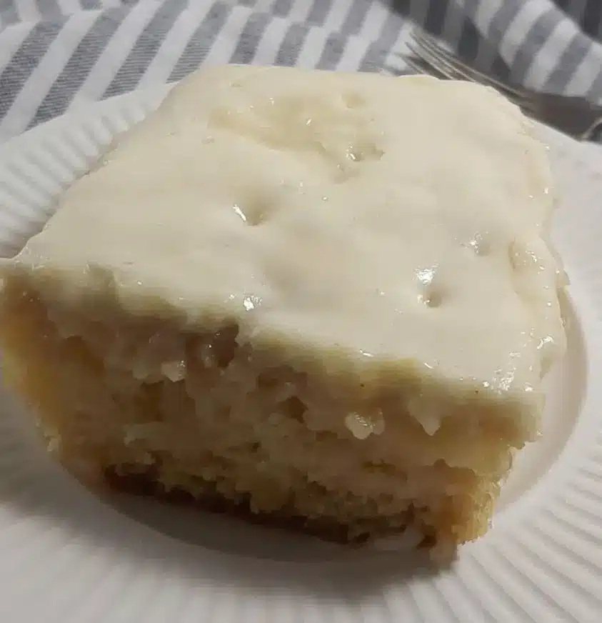 A finished slice of moist pineapple cake with thick cream cheese frosting and pecan garnish