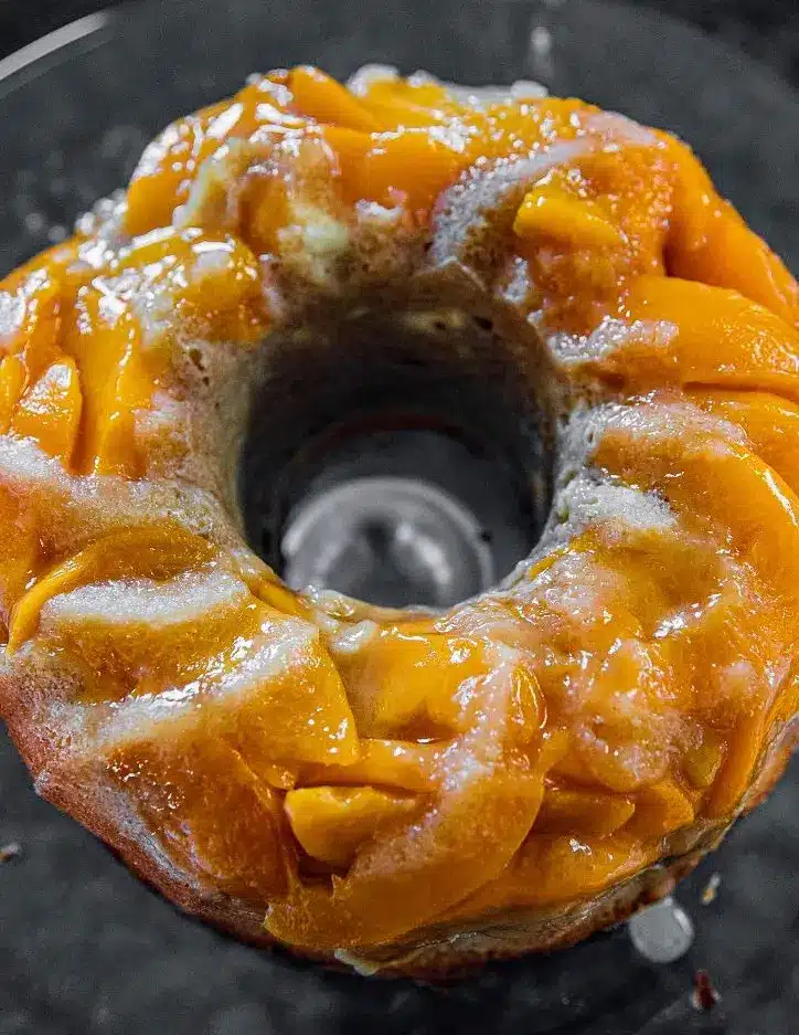 A whole peach cobbler pound cake with a vanilla glaze dripping down the sides.