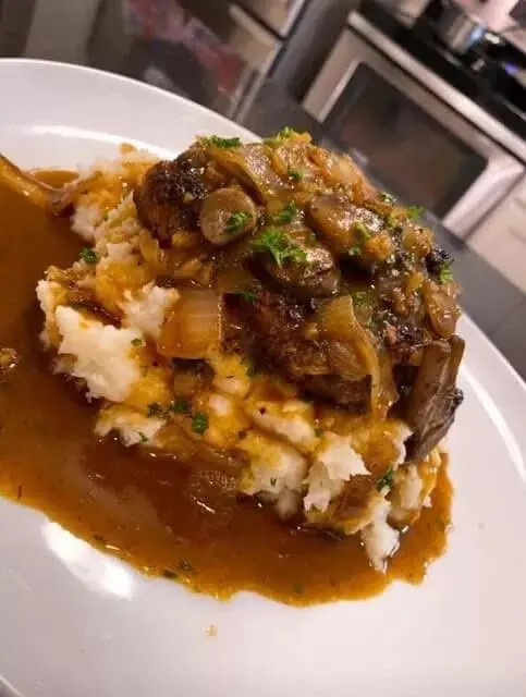 Plated Salisbury steak with onion gravy served next to creamy mashed potatoes and green beans.