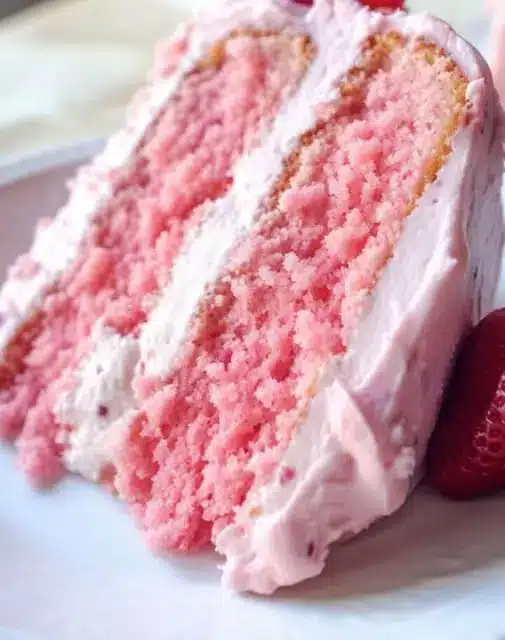 A slice of strawberry layer cake on a plate showing the moist crumb and pink layers