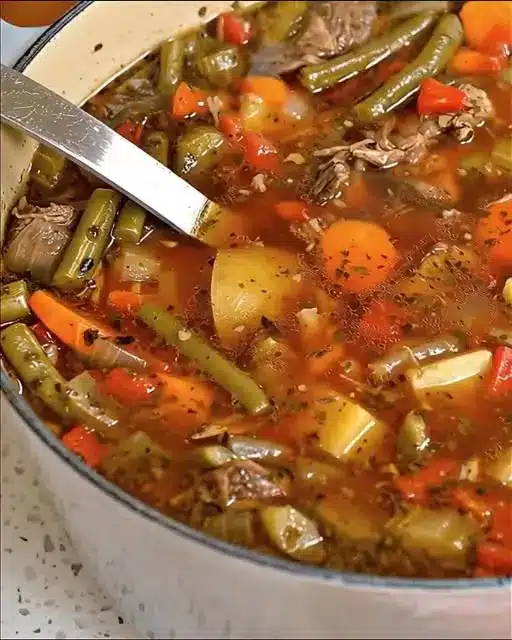 A close-up of vegetable beef soup in a pot, showing tender beef and mixed vegetables in a rich broth