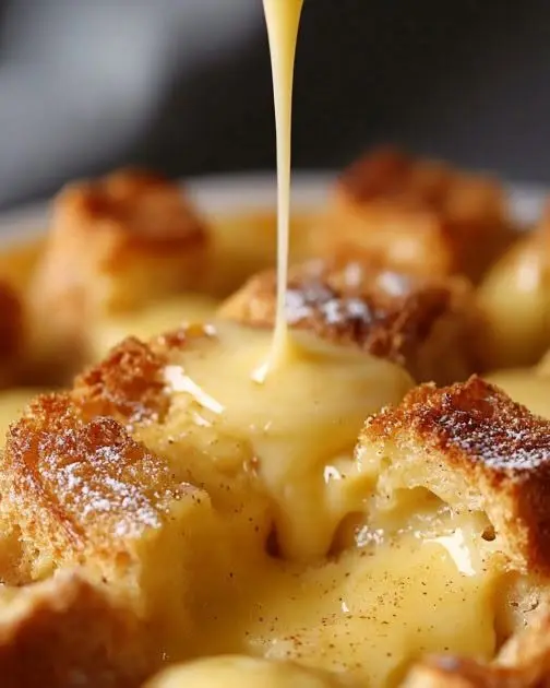 Warm bread pudding sliced and drizzled with a thick vanilla cream sauce
