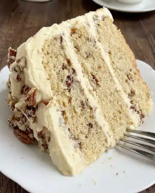 A slice of butter pecan cake on a white plate showing the moist crumb and nut pieces