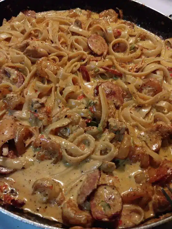 The finished Cajun shrimp sausage pasta garnished with parsley in a large skillet