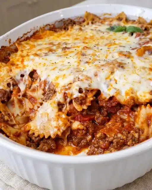 A serving of cheesy baked bowtie pasta on a plate next to a piece of garlic bread.