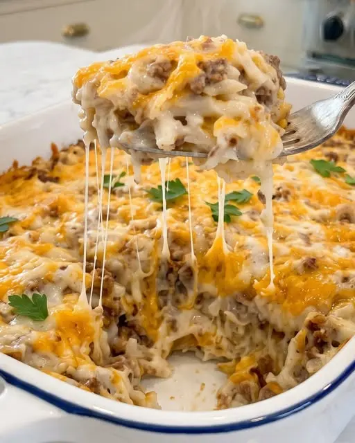 A serving of cheesy hamburger hashbrown casserole on a white plate with steam rising