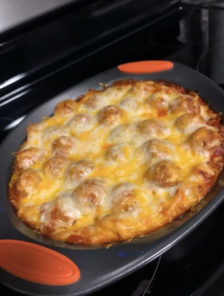 A serving of meatball and potato casserole on a white plate with a side of greens.