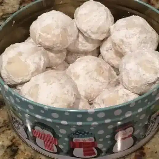 A pile of snowball cookies on a white plate ready to be served