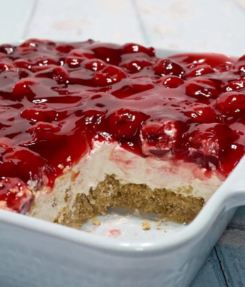 A full dish of cherry delight with a slice removed, showing the distinct layers of graham cracker, cream, and cherries