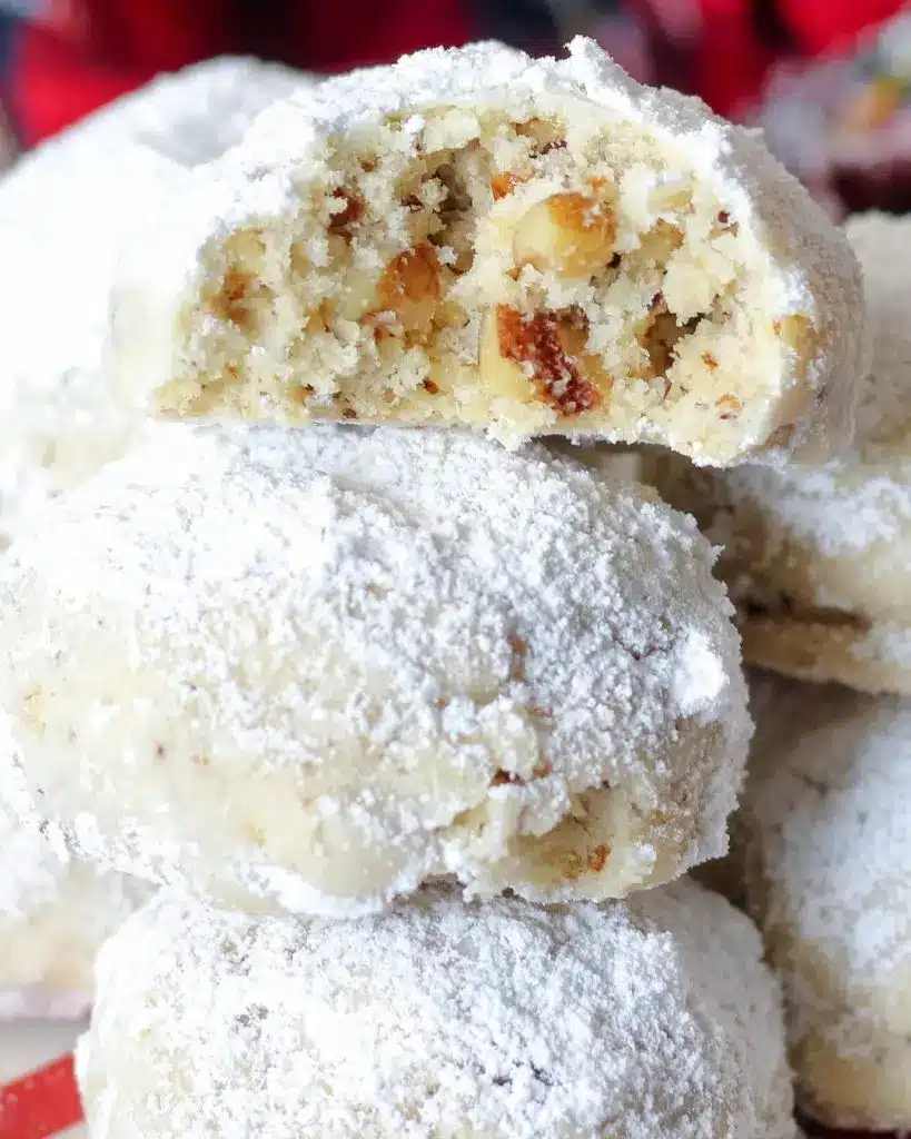 A pile of finished Russian tea ball cookies showing the thick white powdered sugar coating on a festive background.